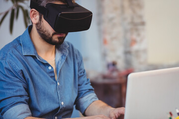 VR headset resting on laptop keyboard inside loft-style workspace with brick wall and potted plant