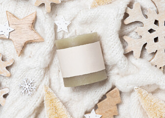 Green pillar candle with blank label on white sweater near wooden Christmas decor, mockup