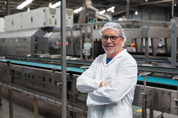 Senior man wearing lab coat and hair net inspecting conveyor belt in production hall, copy space