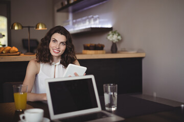 Woman in early thirties holding tablet, smiling at coffee shop table with laptop and orange juice