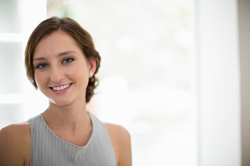Woman standing by bright window wearing sleeveless top and stud earrings smiling, looking at camera