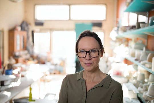 Woman wearing black framed glasses and green shirt, organizing pots and tools in pottery workshop