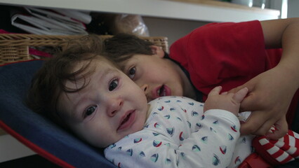 Older brother showing overzealous affection, smothering baby sibling with close contact, baby...