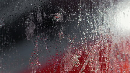 Raindrops and condensation creating a sparkling effect on glass, red and dark background visible through streaks and droplets, abstract scene with water patterns and reflections