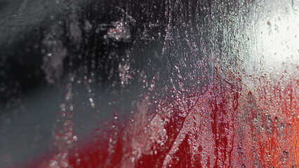 Raindrops and condensation creating a sparkling effect on glass, red and dark background visible through streaks and droplets, abstract scene with water patterns and reflections