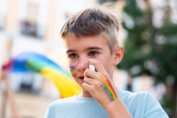 Young boy painting rainbow flag on his face at pride parade