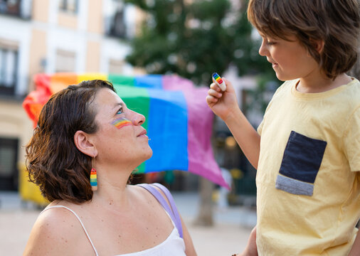 Child painting rainbow on mother's face at pride parade
