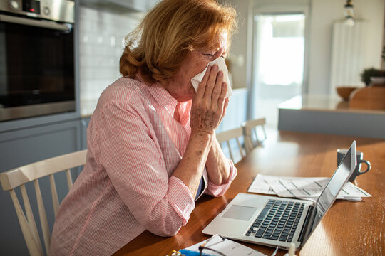 Senior woman working from home with cold or allergies at laptop