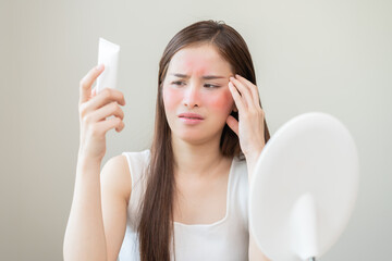 Dermatology, asian young woman looking at mirror, holding cream tube in hand, expression worry and...
