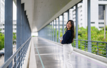 Young Asian businesswoman walking in modern office hallway holding tablet and smiling