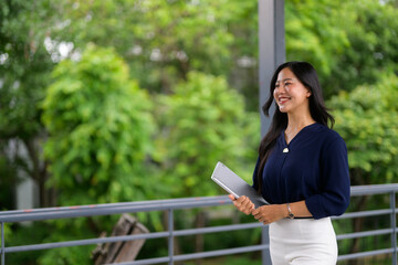 Fototapeta premium Young businesswoman smiling and walking in green corridor holding tablet