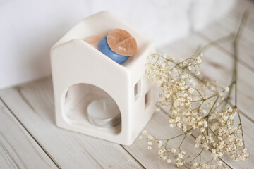 White ceramic wax melter shaped like a house, with candle burning inside and wax melts on top. Surrounded by scented wax bars and candles. Ideal for aromatherapy, home fragrance, and cozy living theme