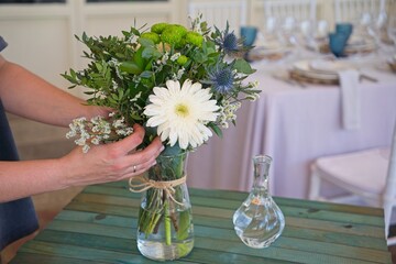 Professional florist woman arranging white gerberas, green chrysanthemums, and mixed blooms in...