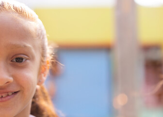 Girl smiling and gazing at camera by wooden post near pastel walls in courtyard, copy space