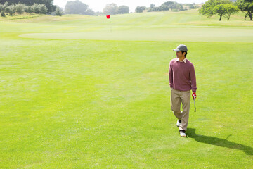 Golfer walking across vibrant green fairway toward red flag, holding putter with red glove