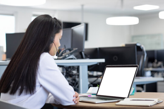 Office worker wearing headset typing on laptop at desk amid monitors in office with LED lights