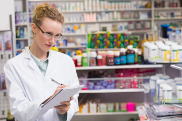 Female pharmacist writing on notepad with pen at pharmacy counter wearing lab coat, copy space