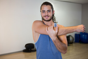Man wearing blue sleeveless top stretching arm across chest in fitness studio with stability balls