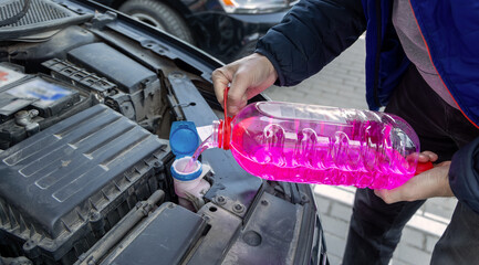 Man Refilling Car Windshield Washer Fluid. Close-up of a person pouring bright pink windshield...