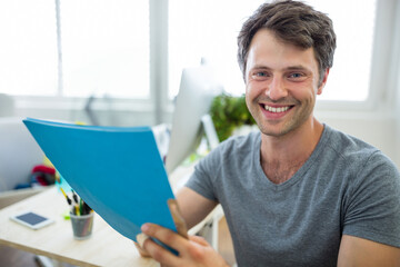 Blue folder resting beside desktop monitor with smartphone and potted plant near window, copy space