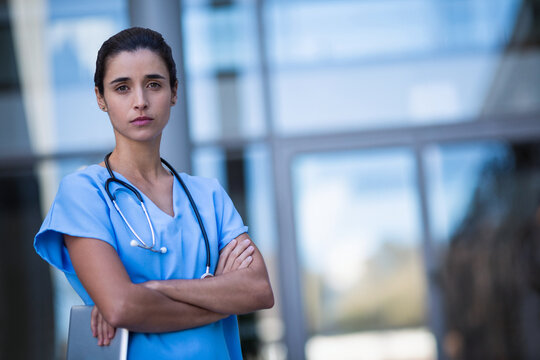 Female nurse standing outside hospital wearing scrubs with tablet and stethoscope, copy space