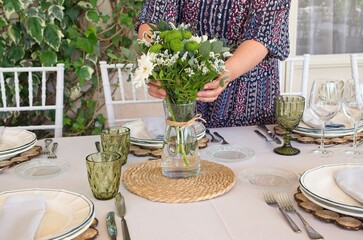 Florist arranging a stunning bouquet of white and green flowers in a glass vase, enhancing a beautifully decorated table for a festive occasion