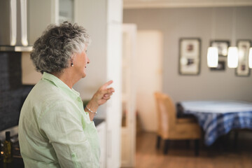 Senior woman pointing toward dining space in kitchen, showing olive oil, checkered tablecloth