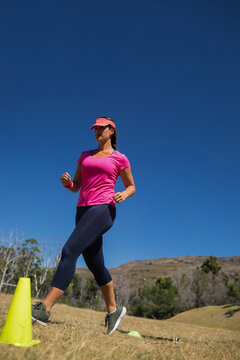 Fototapeta Fitness enthusiast stepping forward between yellow cones on grassy hillside under clear blue sky