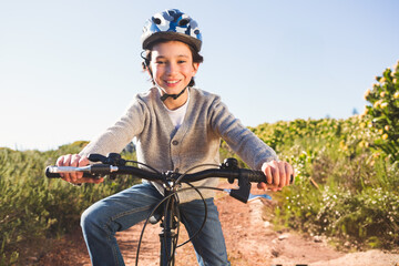 Boy wearing polka-dot helmet riding bicycle along sunlit dirt trail between shrubs under clear sky