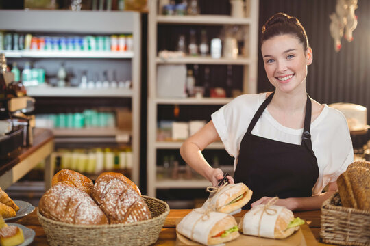 Woman bakery attendant wearing black apron arranging bread loaves in baskets on counter, copy space