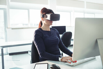 Virtual reality headset resting on white desk near monitor and tablet under natural light in office