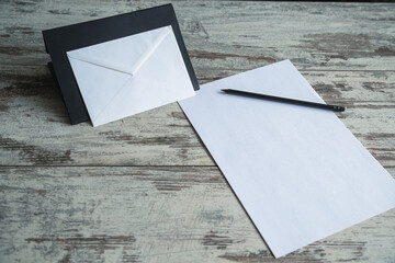 A white envelope on a black stand with paper and a pencil on a wooden table.