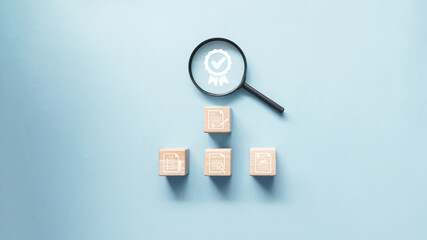 Magnifying glass on certificate icon and wooden block with document icon on it. Concept of document management for quality control check and quality assurance certification.