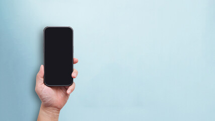 Man hand holding phone in black empty screen for mobile app mockup in blue pastel color background in concept of phone mockup for application with copy space for text.