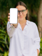 Smiling woman showing smartphone with blank screen outdoor. Mockup for app, website, or social media design.
