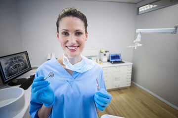 White female dentist holding dental mirror and explorer probe in treatment room with x-ray monitor