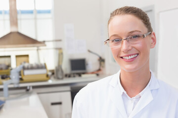 Fototapeta premium Female lab technician wearing white lab coat analyzing sample at bench with fume hood, copy space