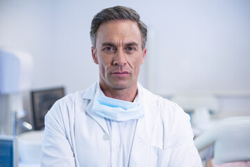 Male doctor standing in exam room wearing white lab coat, surgical mask by computer monitor