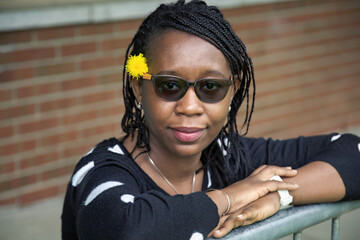 Stylish African Woman with Sunglasses and Yellow Flower Leaning on Railing