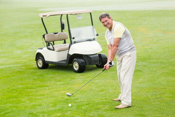 Senior African American man preparing to swing club at golf ball on fairway beside golf cart