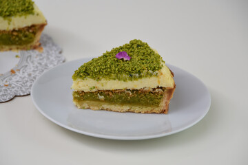 Delicious Pistachio Cheesecake slice presented on a white plate covered with finely ground pistachios and purple flower petals side view of elegant dessert