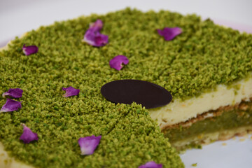 Delicious Pistachio Cheesecake on a pink cake stand covered with finely ground pistachios and purple flower petals closeup side view of elegant dessert