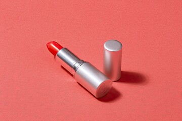 Silver lipstick tube with red lipstick cap off lying on a textured reddishbrown surface