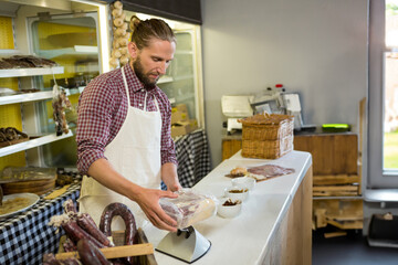 Male butcher handling and weighing vacuum-sealed meat package on digital scale behind counter