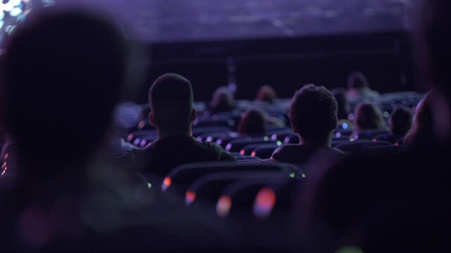 A movie theater full with diverse audience watching an exciting movie back view