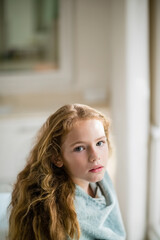 Preteen girl standing near window in bathroom gazing outside with blue towel wrapping shoulders