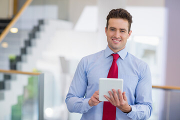 Man standing in office lobby holding tablet wearing dress shirt and necktie near glass railing