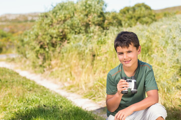 School-aged boy crouching beside dirt path in green shirt and shorts holding binoculars, copy space