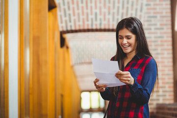 Woman standing in library corridor wearing plaid shirt and reading folded letter, copy space