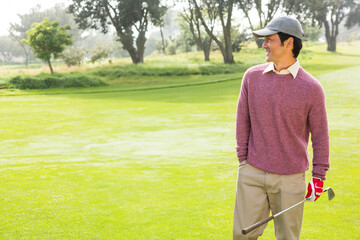 Golfer standing on fairway wearing gray cap and red glove and holding golf club near trees © WavebreakMediaMicro